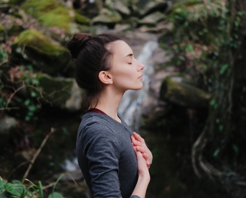 Junge Frau steht in der Natur und atmet bewusst durch