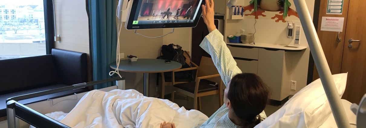 Bettlägrige Patientin bedient Fernsehmonitor am Krankenhausbett